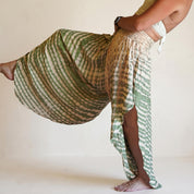 A woman wearing a green and white patterned skirt is striking a pose with one leg extended and the other bent at the knee.