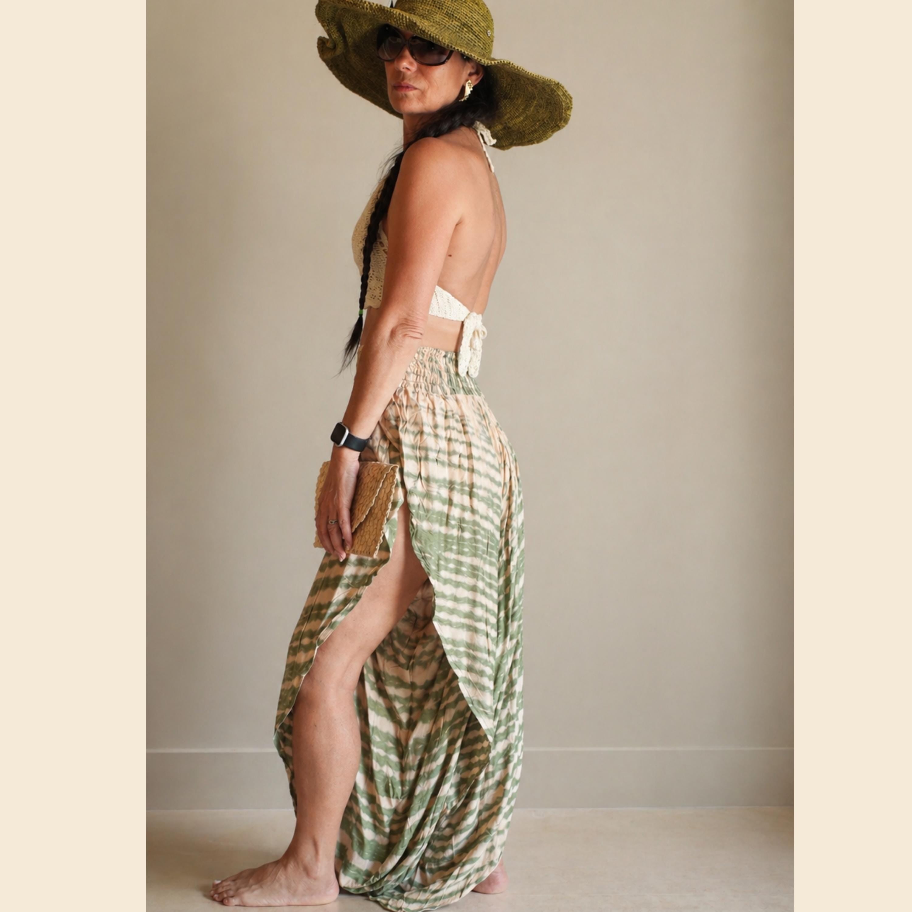 A woman wearing a green hat and a long skirt with a high slit, posing in a studio setting.