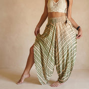 A woman wearing a white crocheted top and a green and beige patterned skirt, posing with her legs apart and her hands in her pockets.