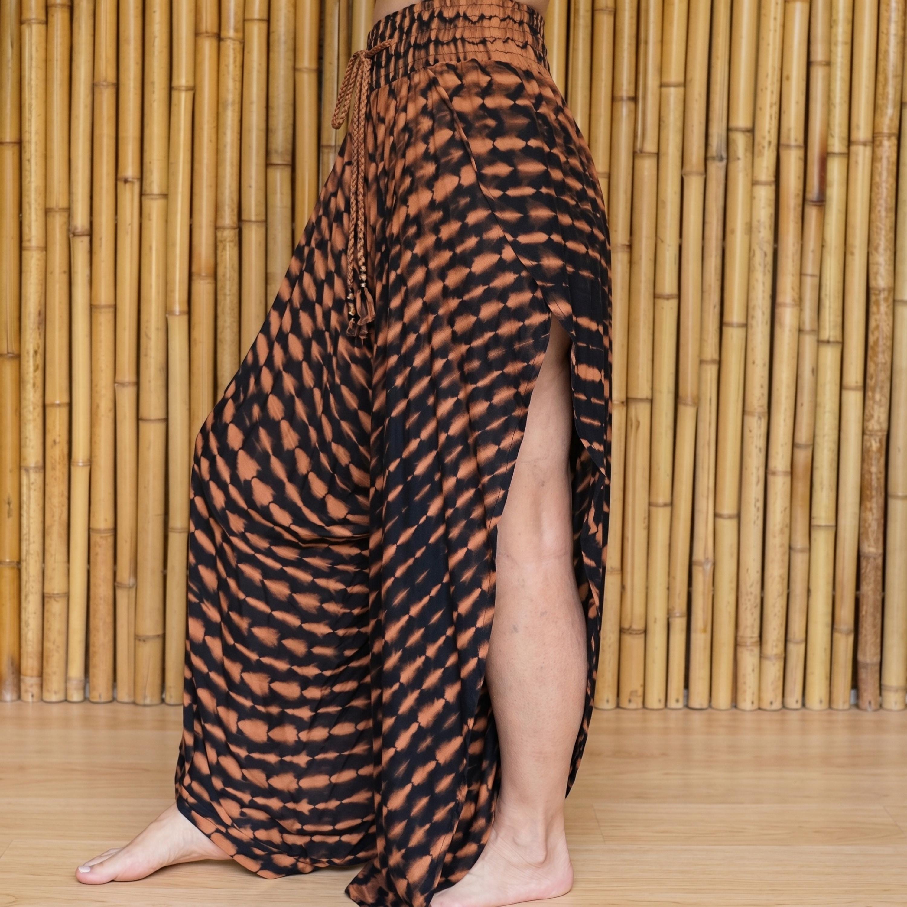 A person wearing a long, patterned skirt with a high slit, standing in front of a bamboo wall.