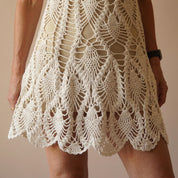 A close-up view of a woman wearing a white crocheted dress with a scalloped hem and intricate lace-like patterns.