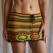A person wearing a colorful, crocheted skirt with a pattern of orange, green, and yellow stripes.