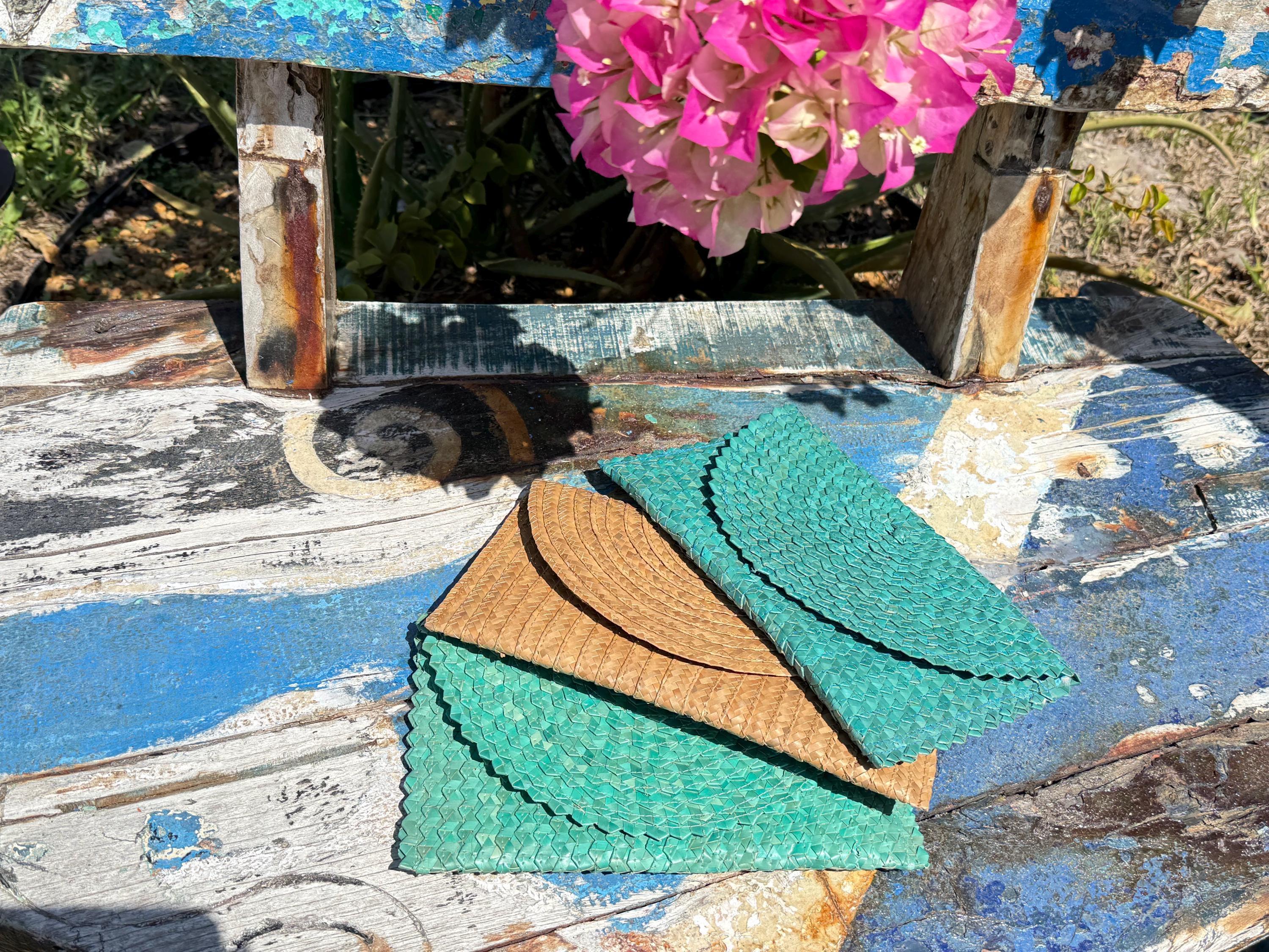 a wooden bench with a blue and white paint, a pink flower, and two folded green and brown bags or purses placed on it.