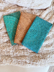 three colorful woven bags or purses, each with a unique pattern and color, resting on a soft, fluffy surface.