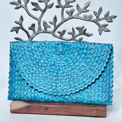 A blue woven purse or clutch with a textured, woven pattern is displayed on a wooden stand.