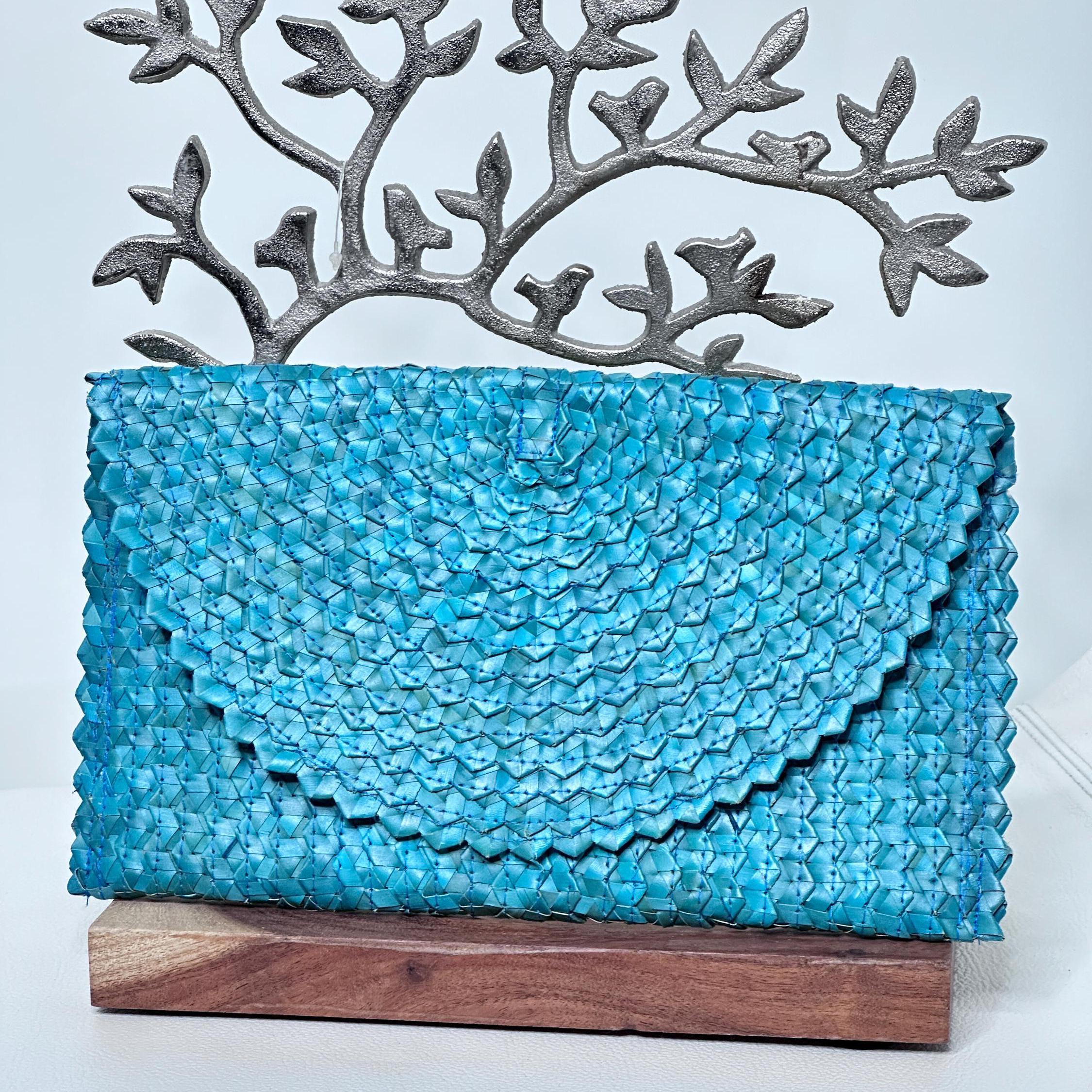 A blue woven purse or clutch with a textured, woven pattern is displayed on a wooden stand.