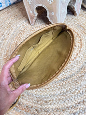 A hand is holding an open, brown purse or bag with a woven texture, placed on a woven mat or rug.