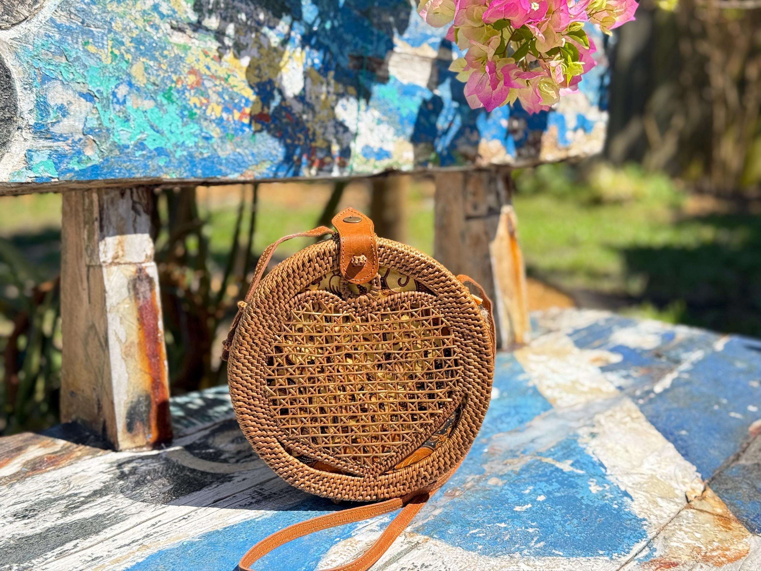 A round woven purse with a heart-shaped pattern sits on a blue bench, with a pink flower nearby.