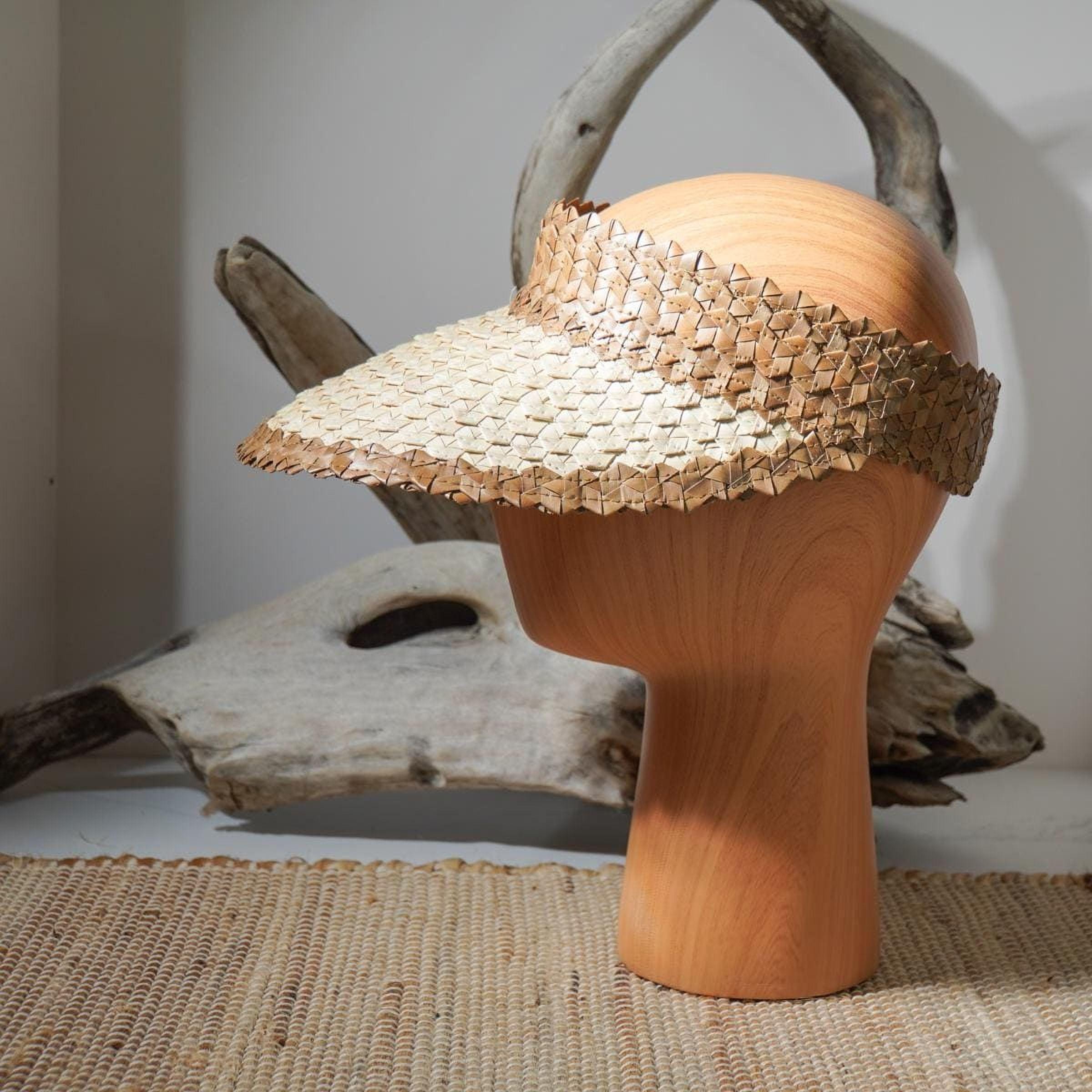 a wooden headless mannequin wearing a straw hat with a woven pattern. The hat is placed on a woven mat, and there is a wooden log or branch in the background.