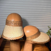 Two wooden mannequins wearing straw hats stand on a wooden surface against a striped background.