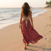 A woman in a red floral skirt walks along a sandy beach, facing away from the camera.