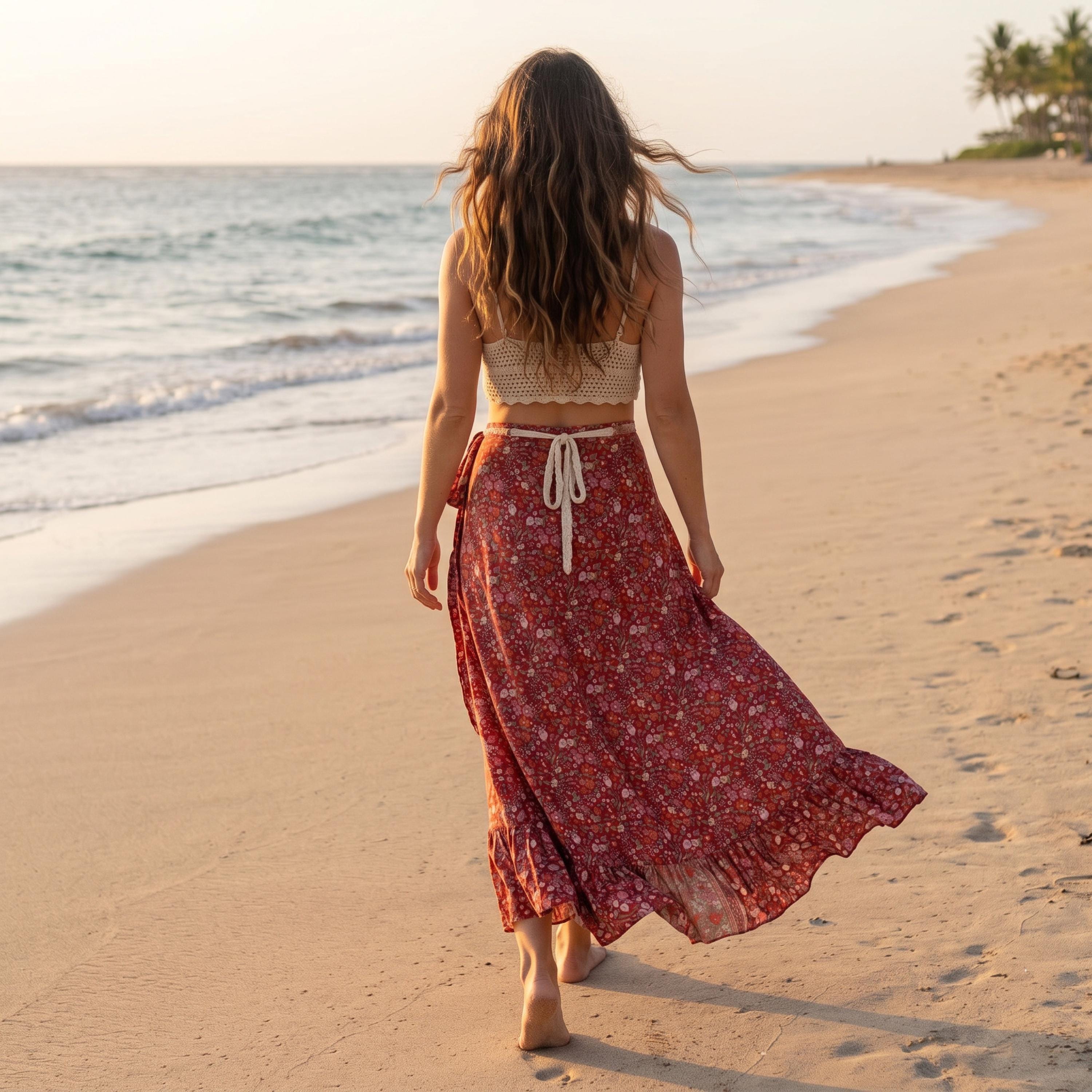 A woman in a red floral skirt walks along a sandy beach, facing away from the camera.