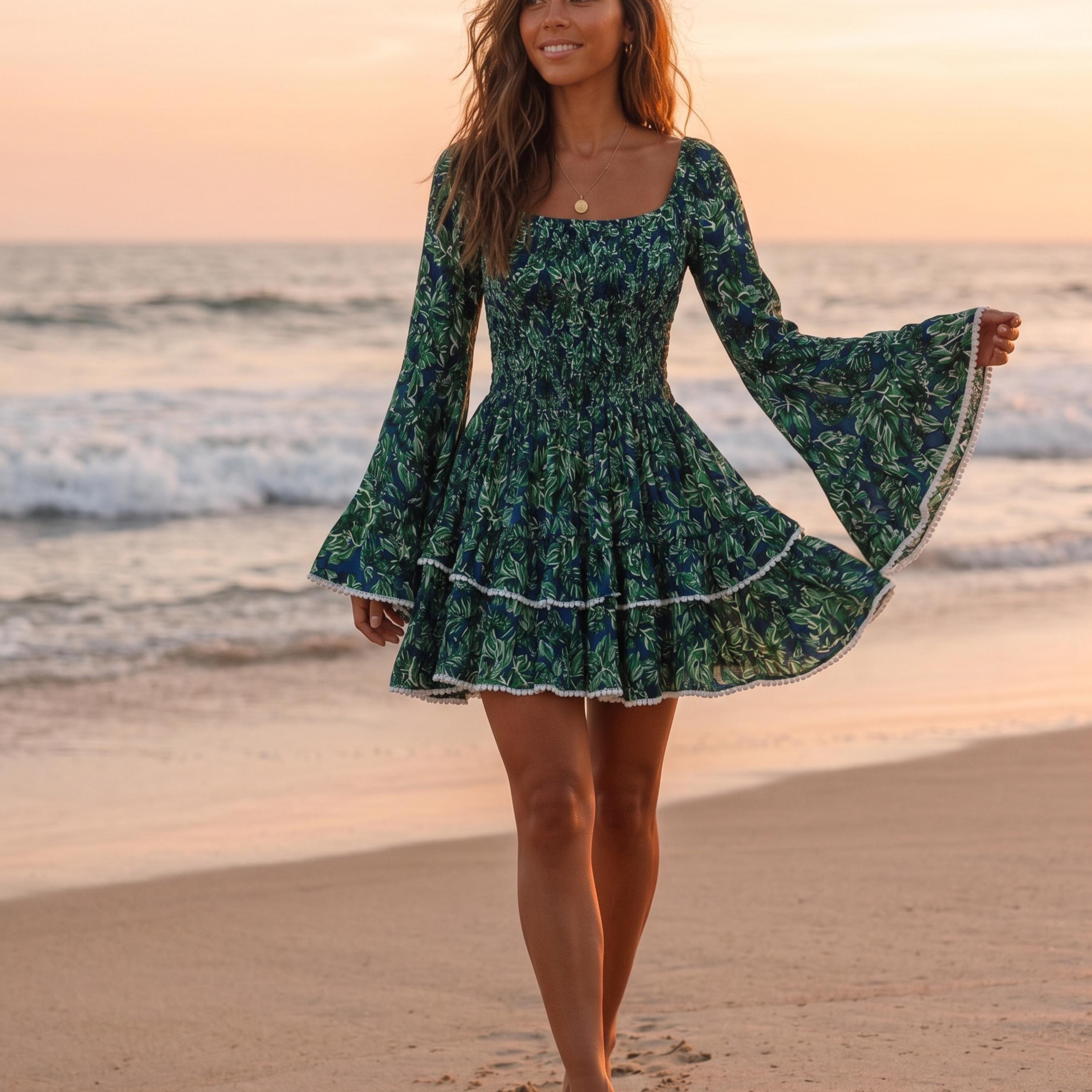 A woman in a green floral dress walks along a beach at sunset, her long hair flowing in the wind.
