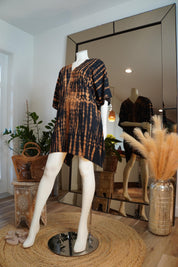 a mannequin wearing a tie-dye dress, placed in a room with a large mirror and various decorative elements such as potted plants and a woven rug.