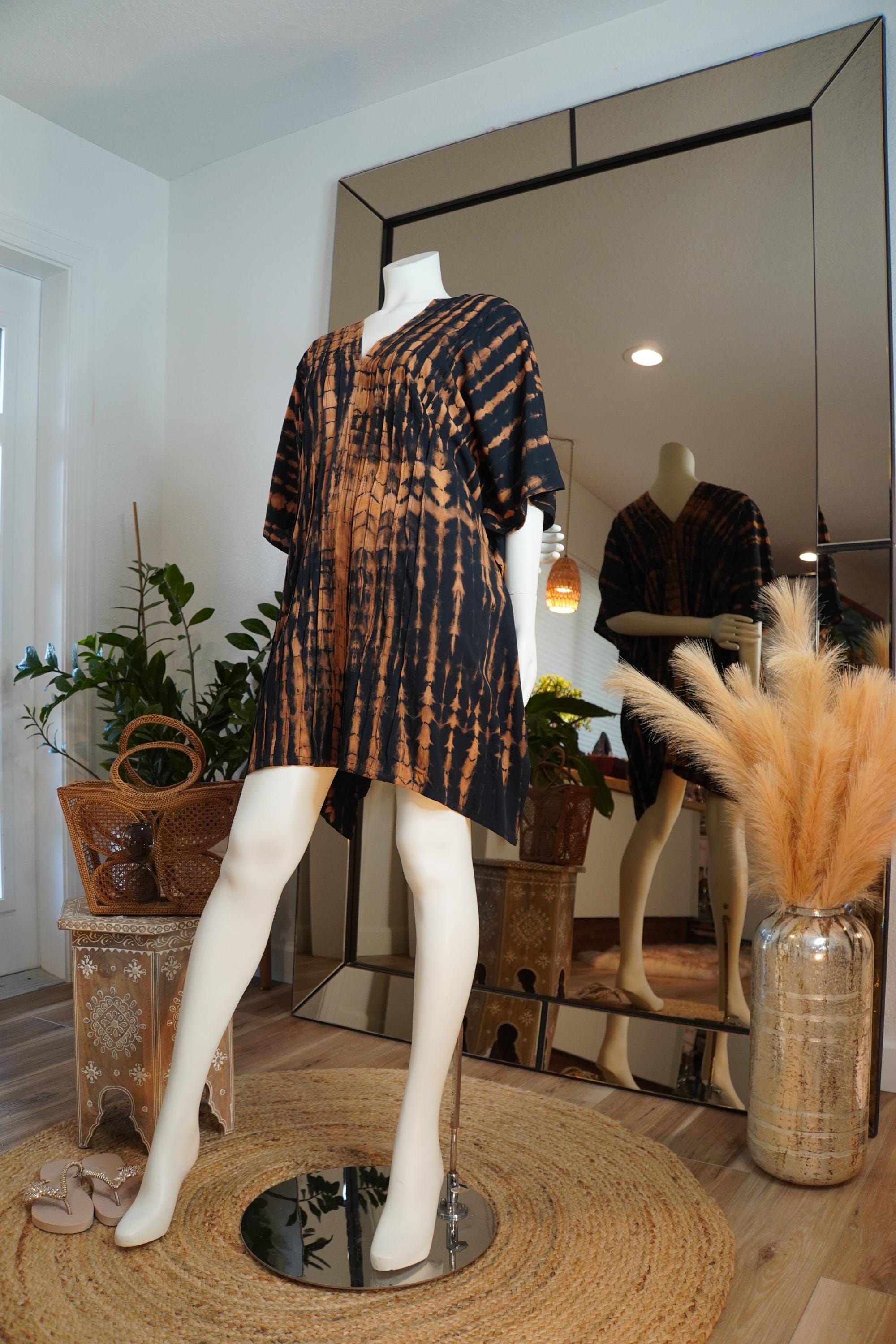 a mannequin wearing a tie-dye dress, placed in a room with a large mirror and various decorative elements such as potted plants and a woven rug.