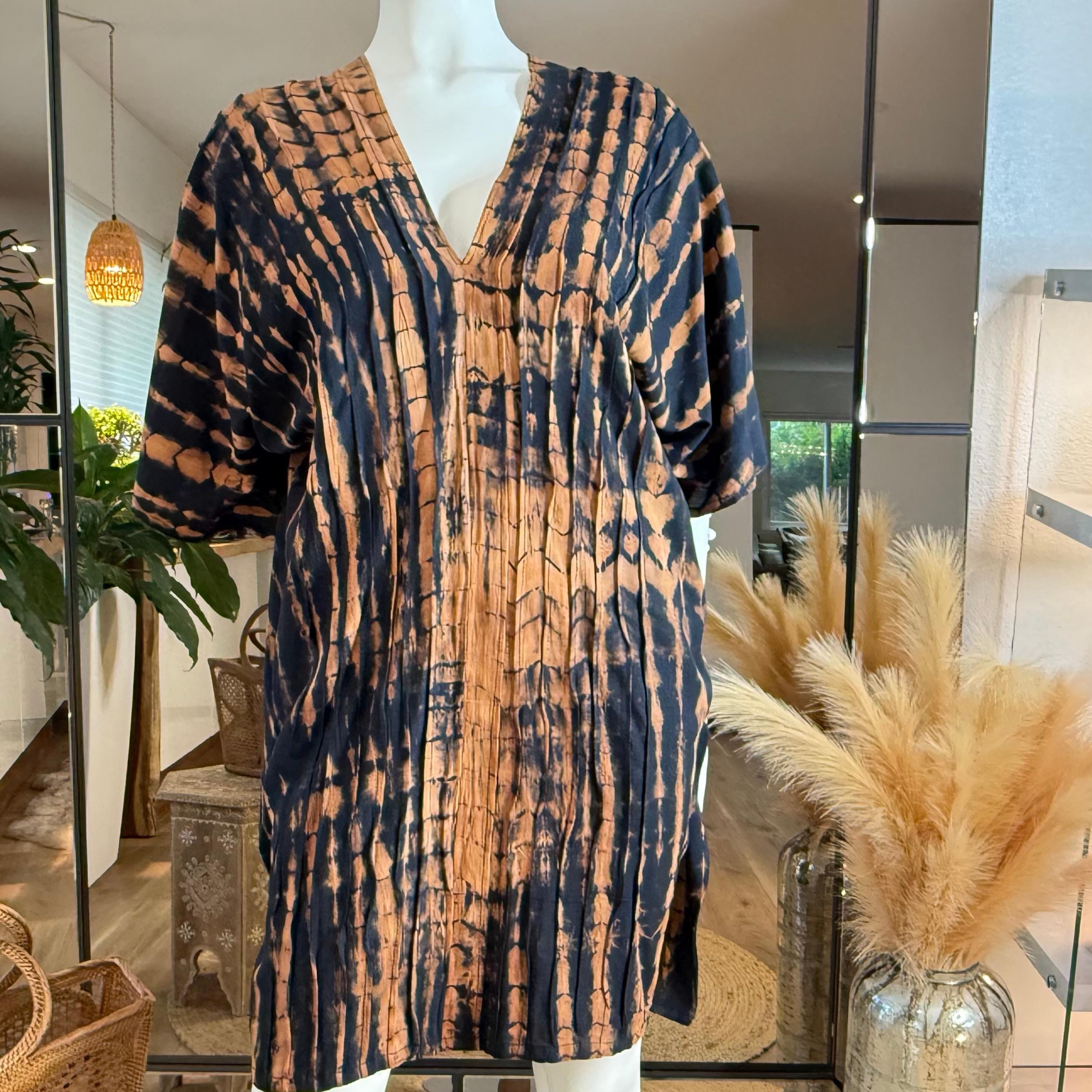 A mannequin wearing a tie-dye dress with a pattern of orange and black stripes, displayed in a room with potted plants and a mirror.