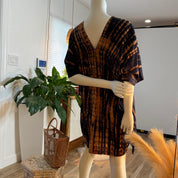 A mannequin wearing a tie-dye dress stands in a room with a potted plant and a woven basket nearby.