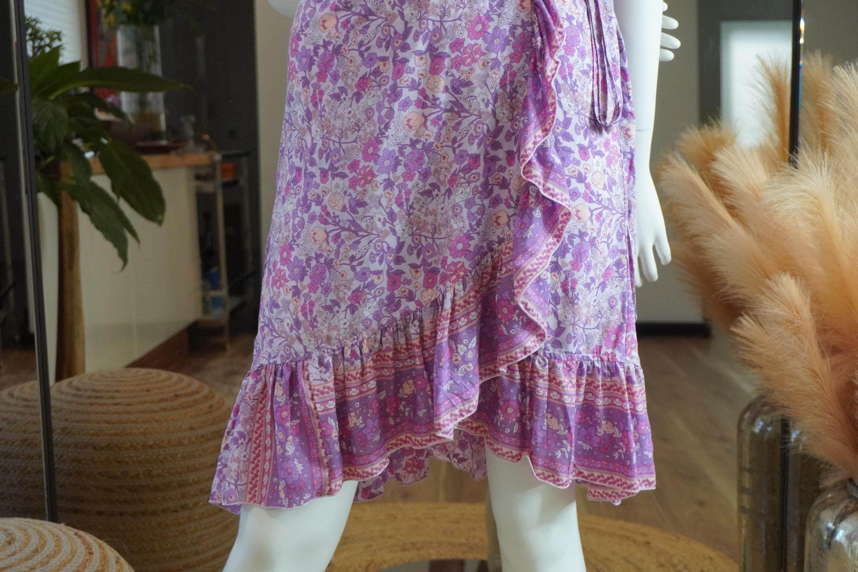 A mannequin wearing a purple floral print skirt with a ruffled hem and a tie at the waist.