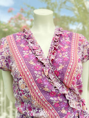 A mannequin wearing a purple and white floral print dress with ruffled details and a wrap-style neckline.