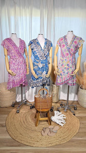 Three mannequins wearing colorful dresses are displayed in a store, with a woven mat in the foreground and some accessories nearby.