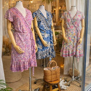 A display of three mannequins wearing colorful dresses in a clothing store window.