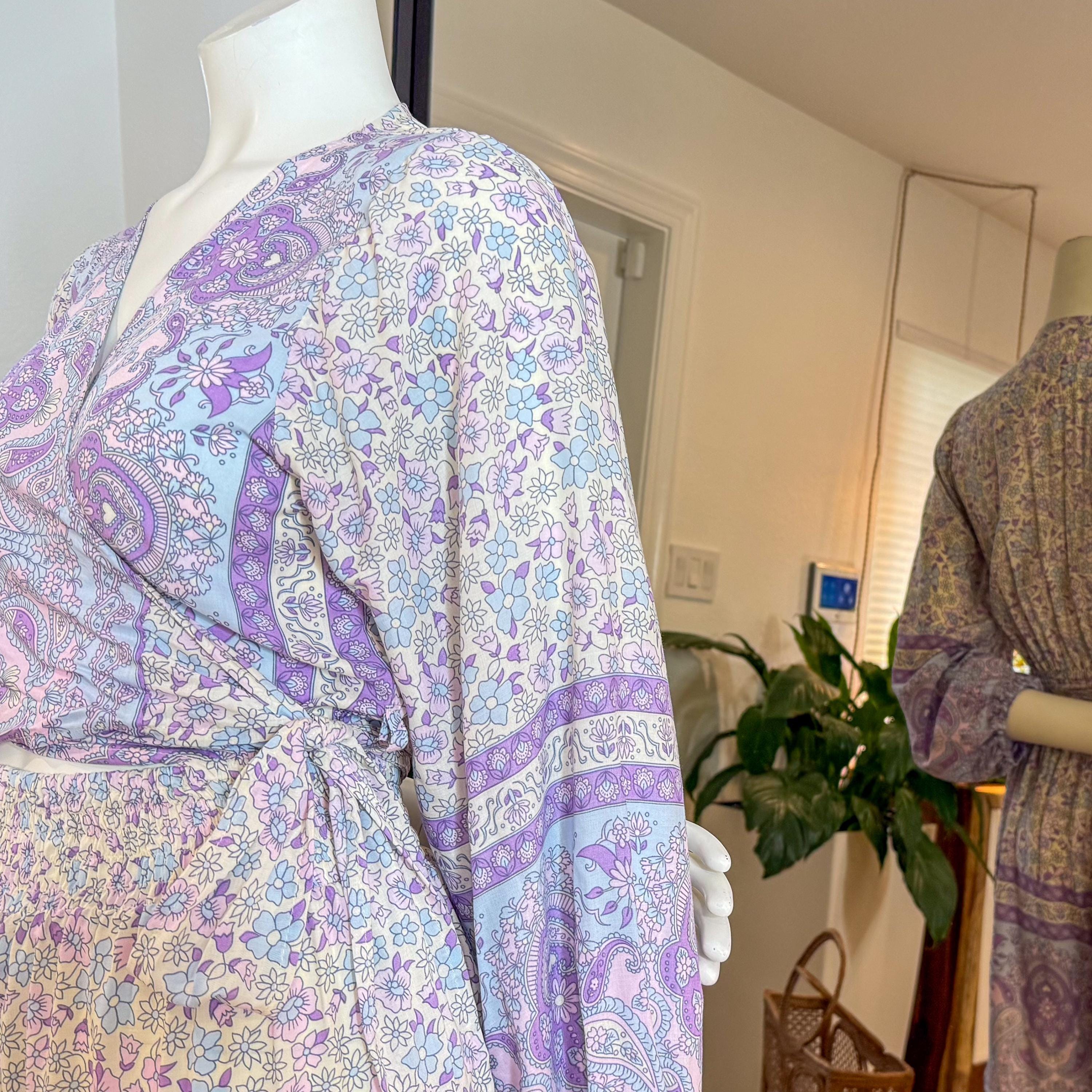 a mannequin wearing a purple and white patterned wrap dress, with a plant in the background.