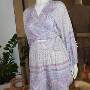 A mannequin wearing a purple and white patterned dress with a wrap top and a skirt, displayed in a clothing store.