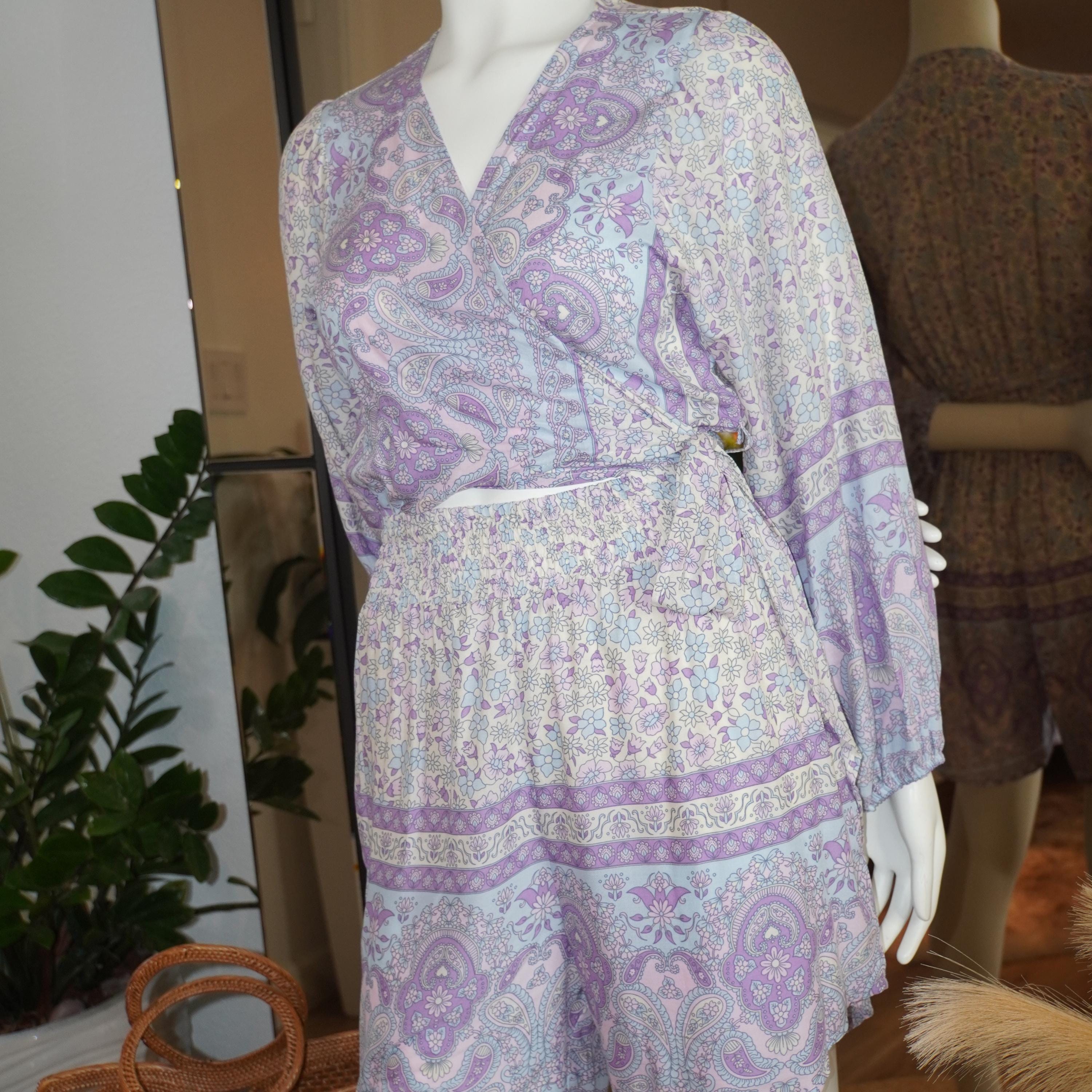 A mannequin wearing a purple and white patterned dress with a wrap top and a skirt, displayed in a clothing store.