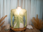 A mannequin wearing a green, long-sleeved top with a scalloped hem, displayed on a wooden stand.
