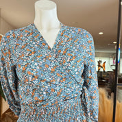 A mannequin wearing a blue and orange floral print dress with a wrap-style neckline and long sleeves.