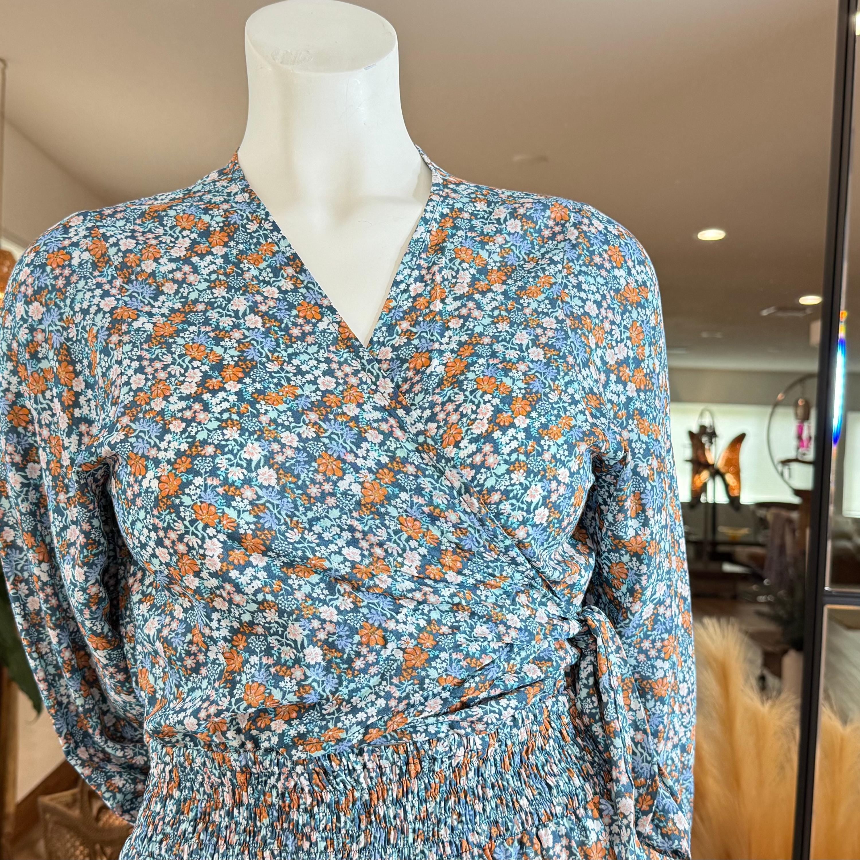 A mannequin wearing a blue and orange floral print dress with a wrap-style neckline and long sleeves.