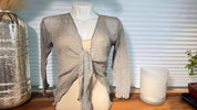 a mannequin wearing a gray knitted cardigan, placed on a wooden surface next to a candle and a decorative vase.