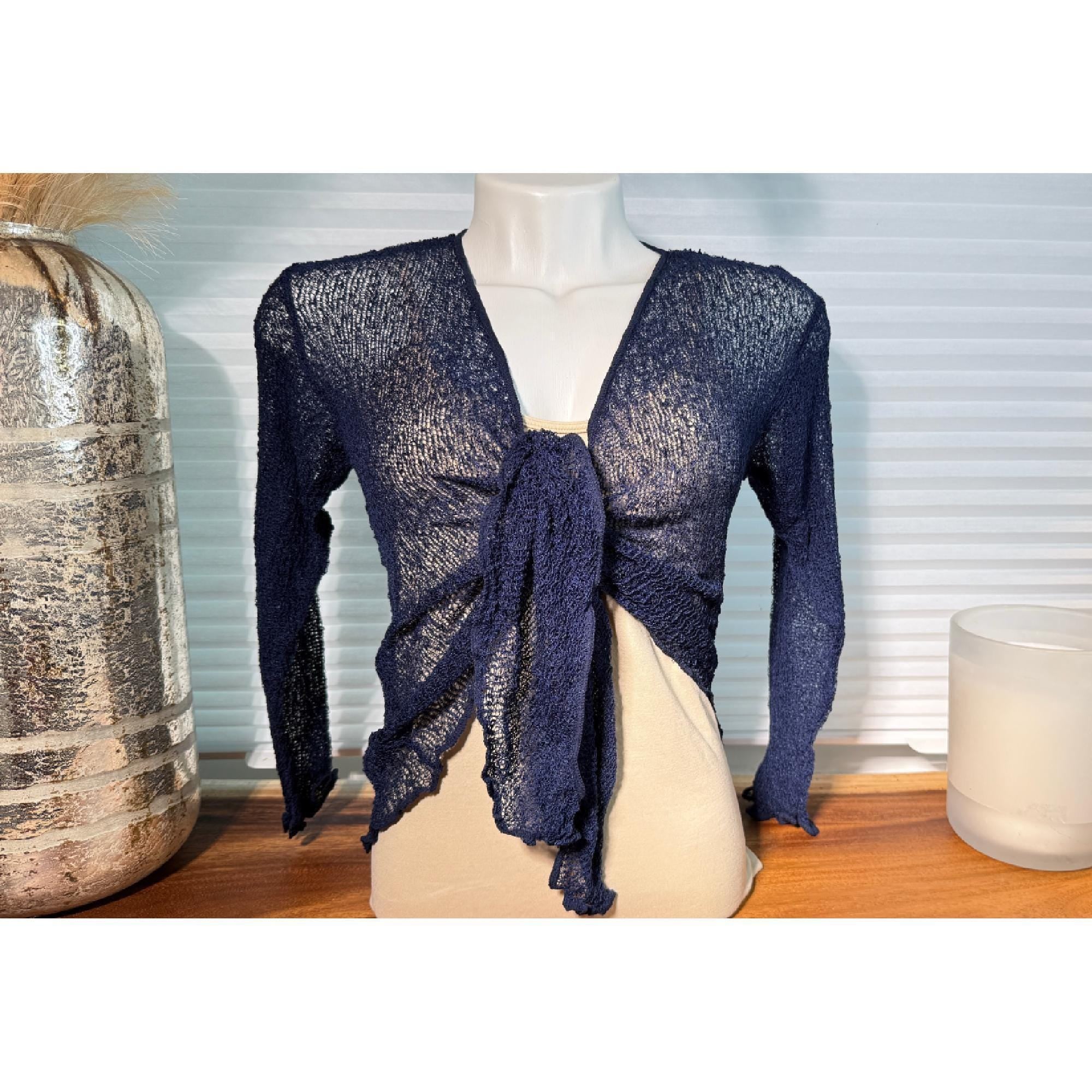 A mannequin wearing a navy blue knitted wrap top with a tie detail, placed on a wooden surface next to a glass vase.