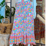 A mannequin wearing a colorful floral skirt with a ruffled hem and a woven purse on a table.