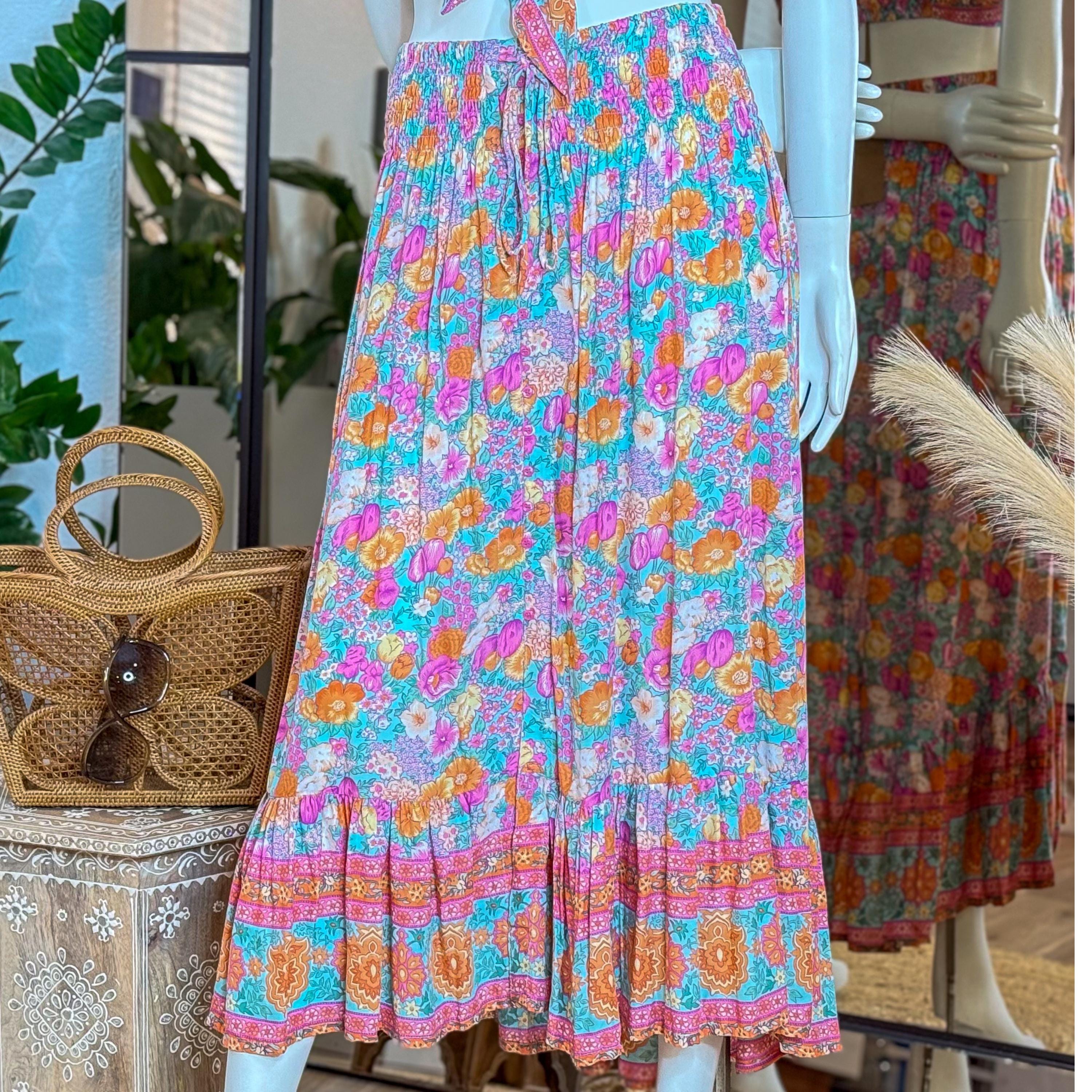 A mannequin wearing a colorful floral skirt with a ruffled hem and a woven purse on a table.