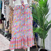 A mannequin wearing a colorful floral print skirt with a ruffled hem, displayed in a clothing store with various other dresses and clothing racks visible in the background.