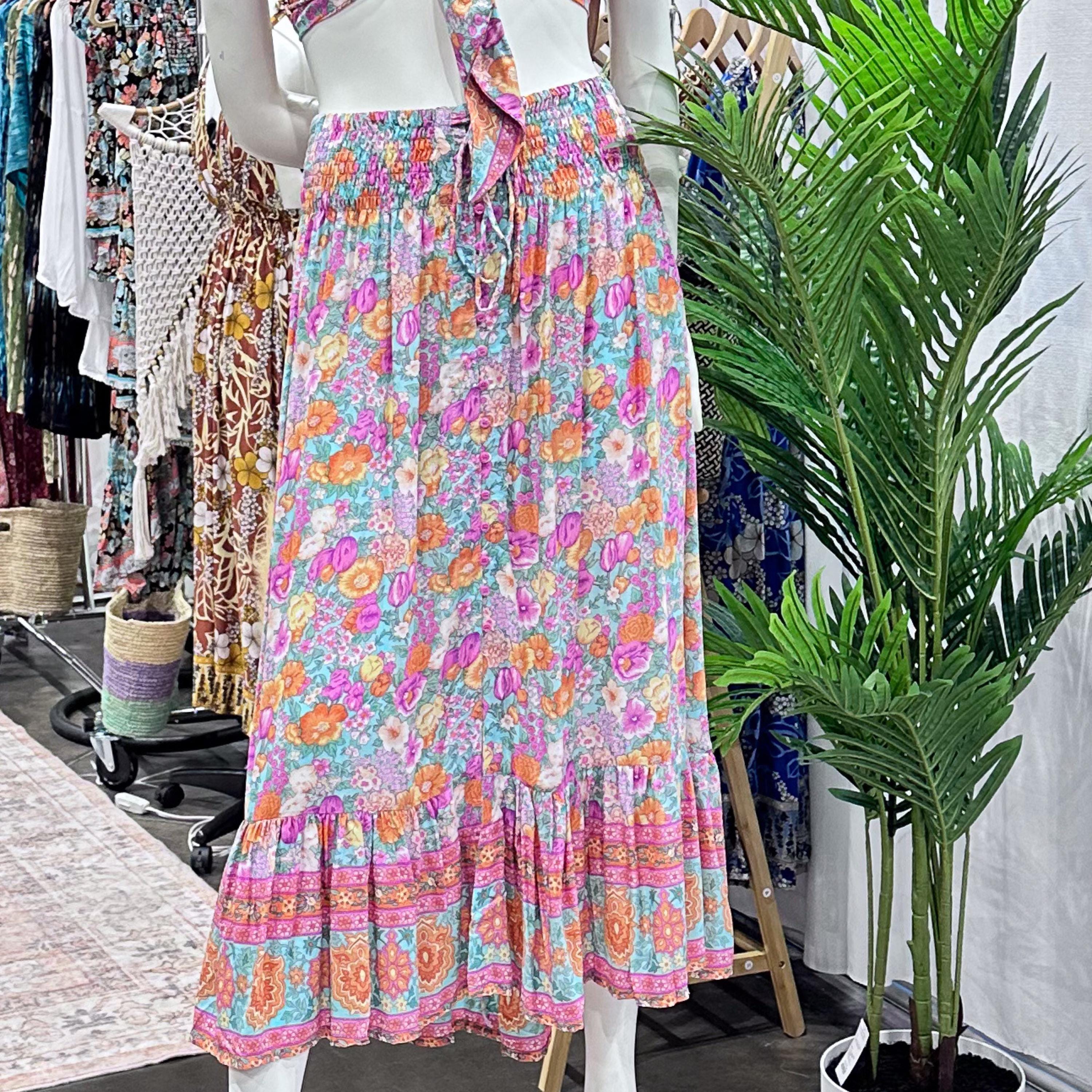 A mannequin wearing a colorful floral print skirt with a ruffled hem, displayed in a clothing store with various other dresses and clothing racks visible in the background.