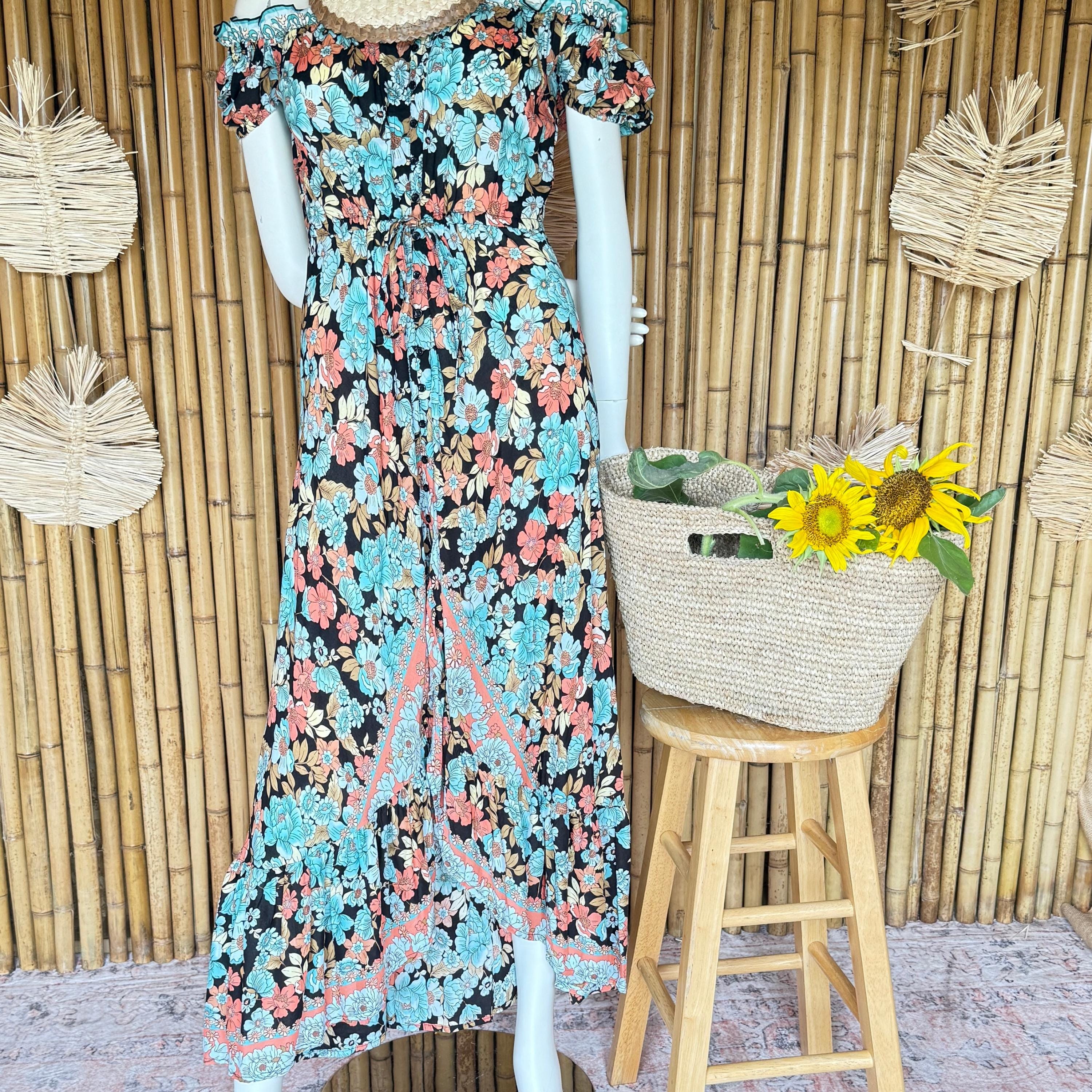 A mannequin wearing a colorful floral print dress stands next to a woven basket filled with yellow flowers, placed on a wooden stool against a bamboo wall.
