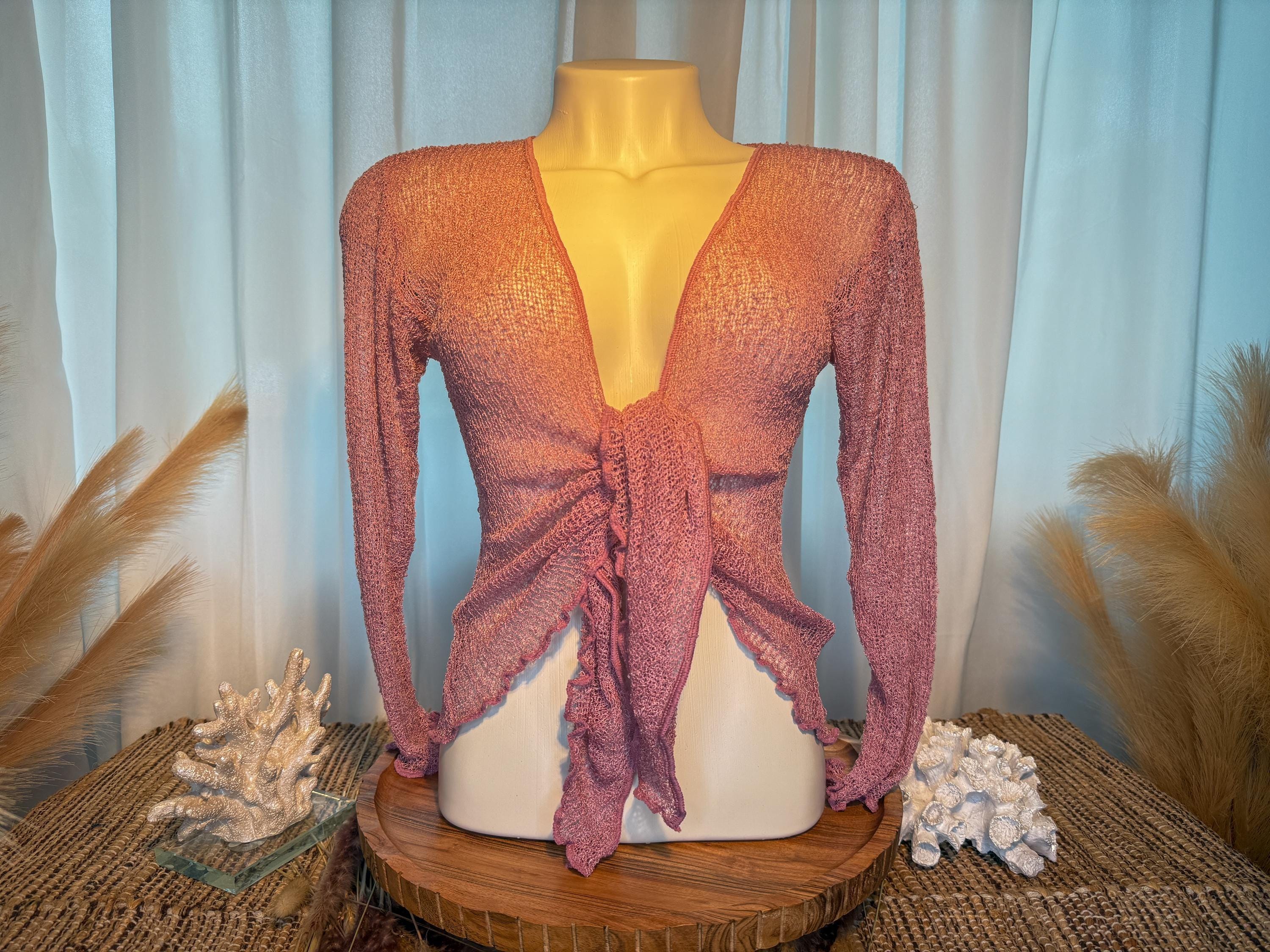 A mannequin wearing a pink knitted top with long sleeves, displayed on a wooden stand with coral and other natural elements in the background.