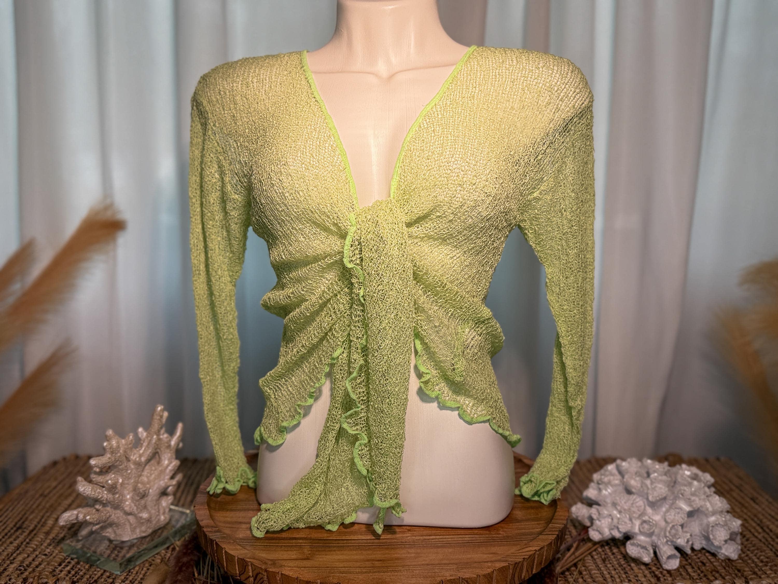 A mannequin wearing a green, ruched blouse with long sleeves, displayed on a wooden stand.