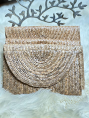 a woven straw purse with a curved shape and a textured pattern, placed on a white fur surface.