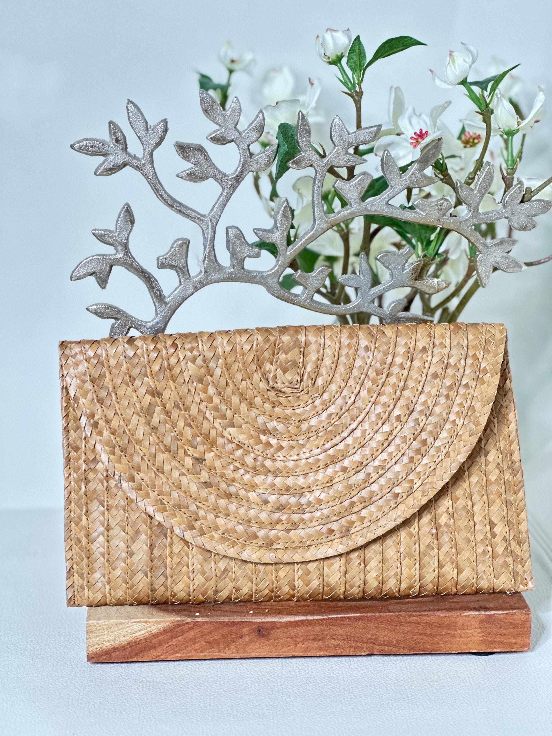 a straw purse placed on a wooden stand, with a vase of white flowers behind it.