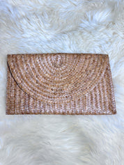 A brown woven clutch purse is placed on a fluffy white surface.