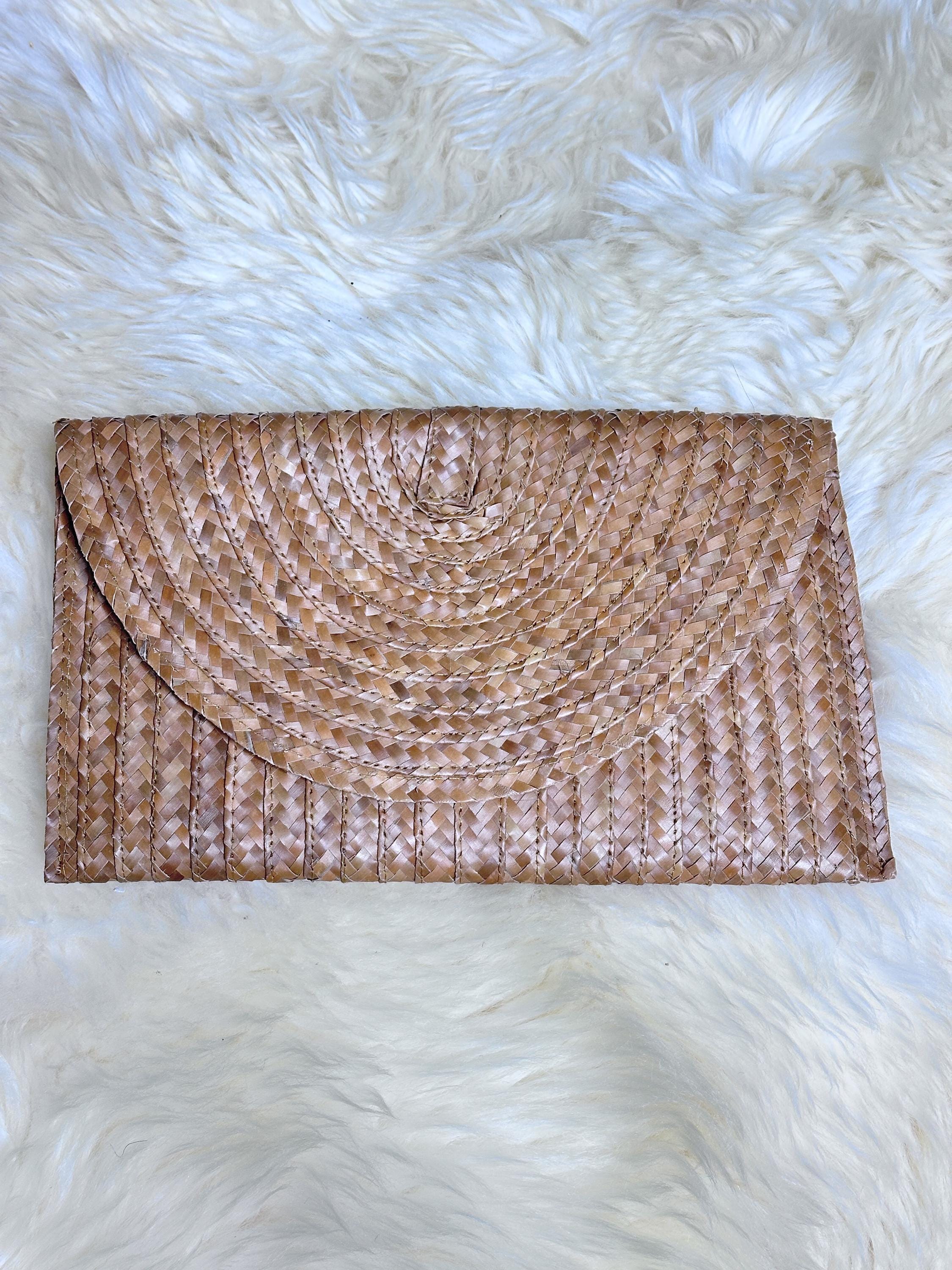 A brown woven clutch purse is placed on a fluffy white surface.