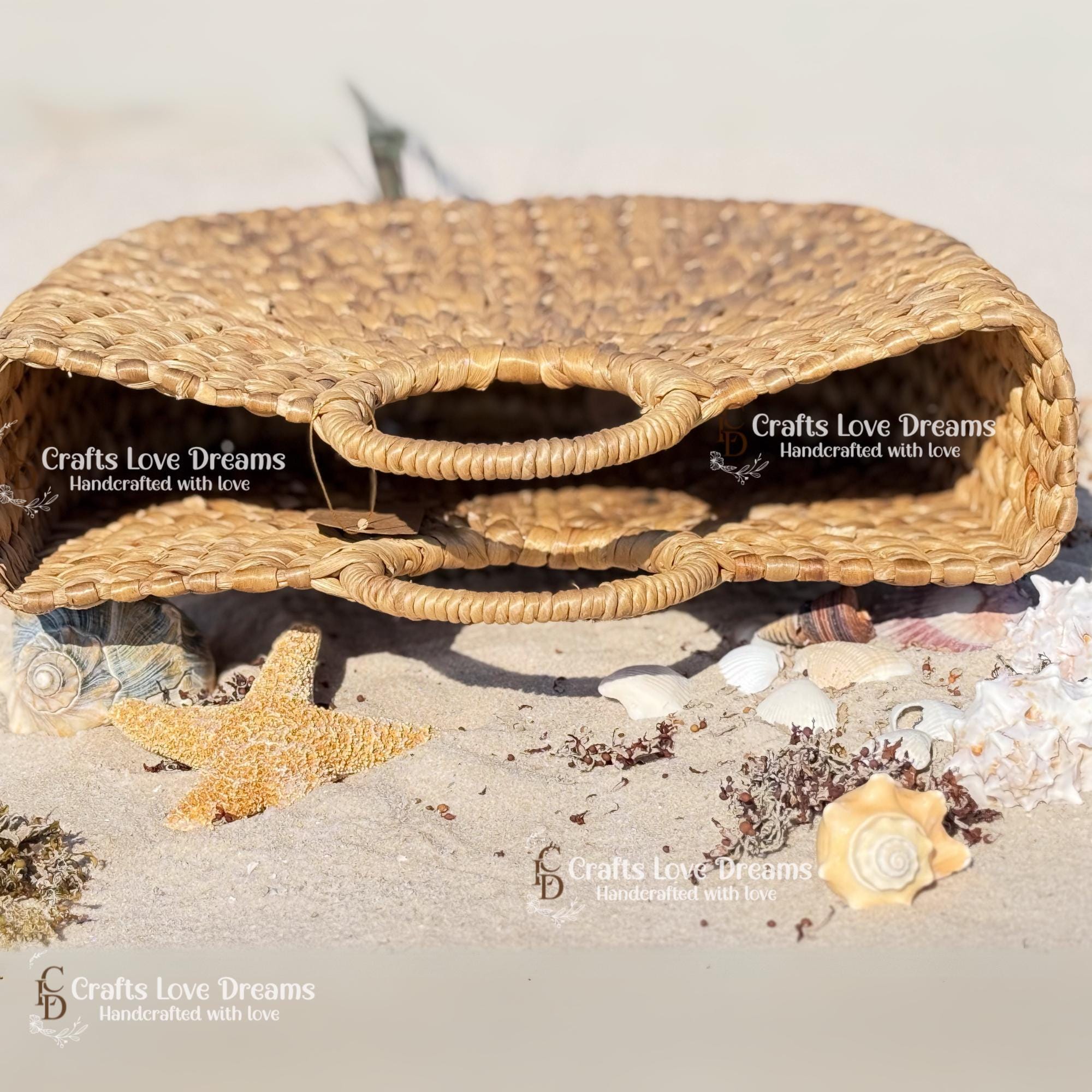 A woven straw bag with handles, placed on a beach with seashells and starfish nearby.