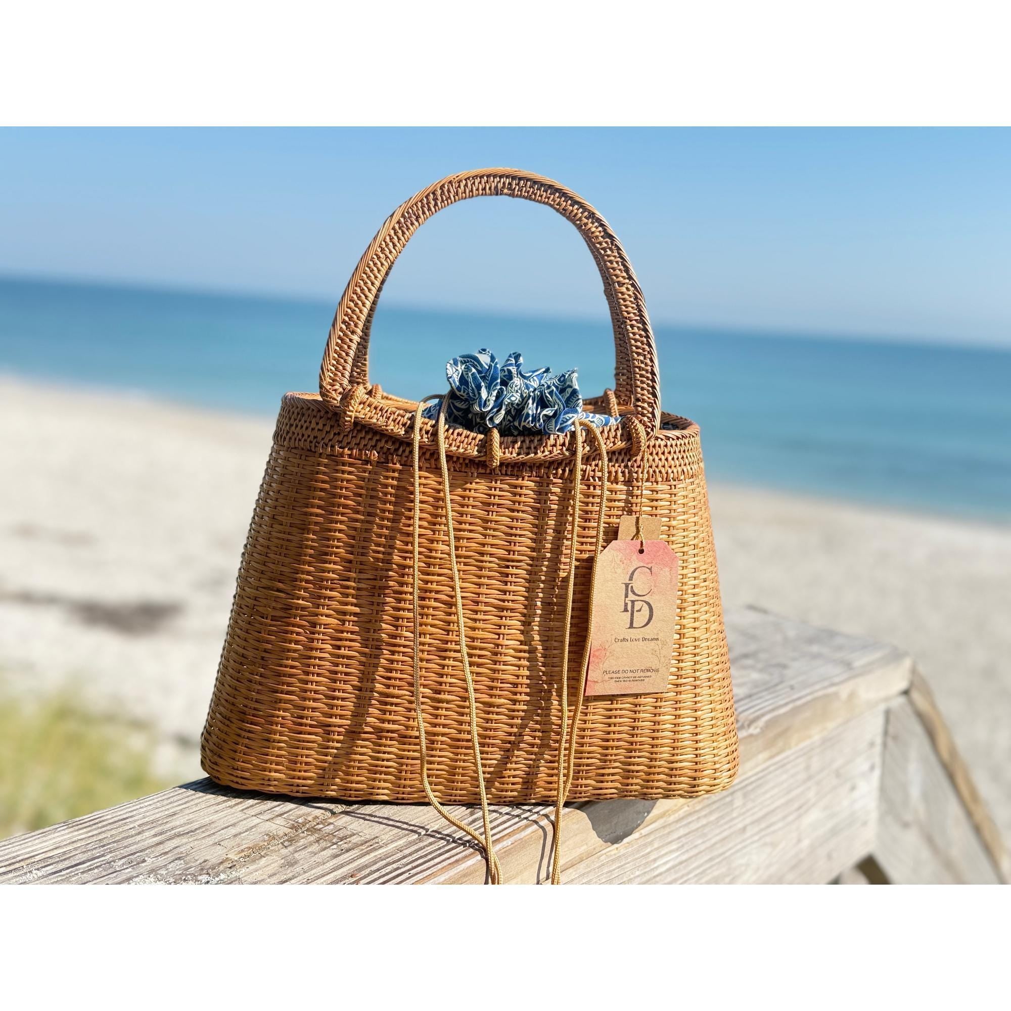 A brown woven handbag with a tag attached, placed on a wooden surface near the ocean.