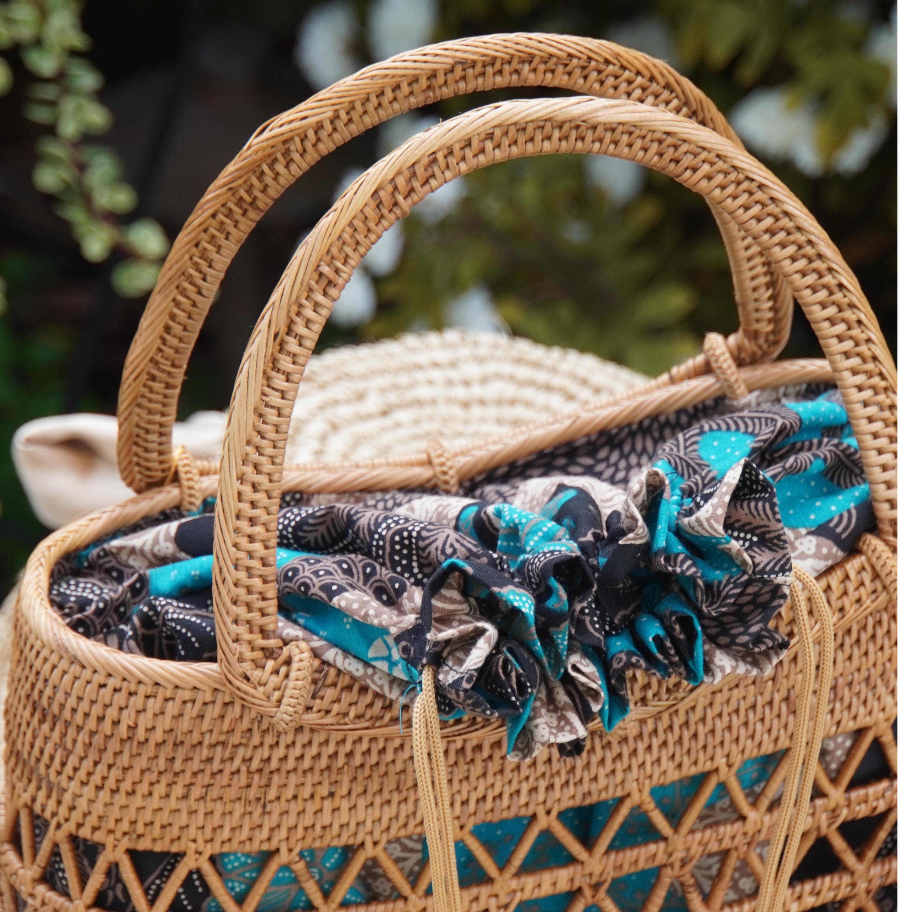 A woven straw bag with a patterned fabric draped over it, placed outdoors against a blurred natural background.