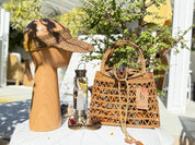 a wooden headband, a woven handbag, a water bottle, and sunglasses arranged on a white table.