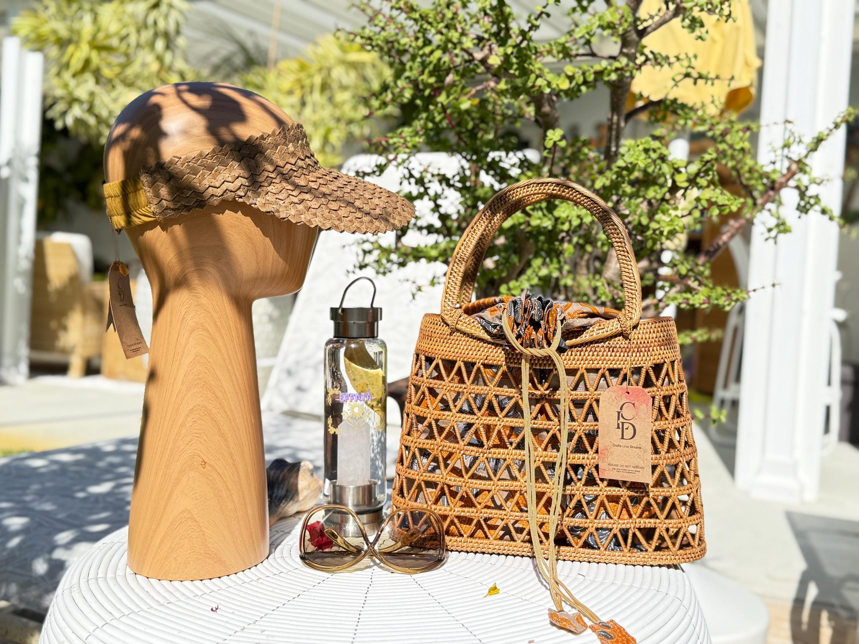 a wooden headband, a woven handbag, a water bottle, and sunglasses arranged on a white table.