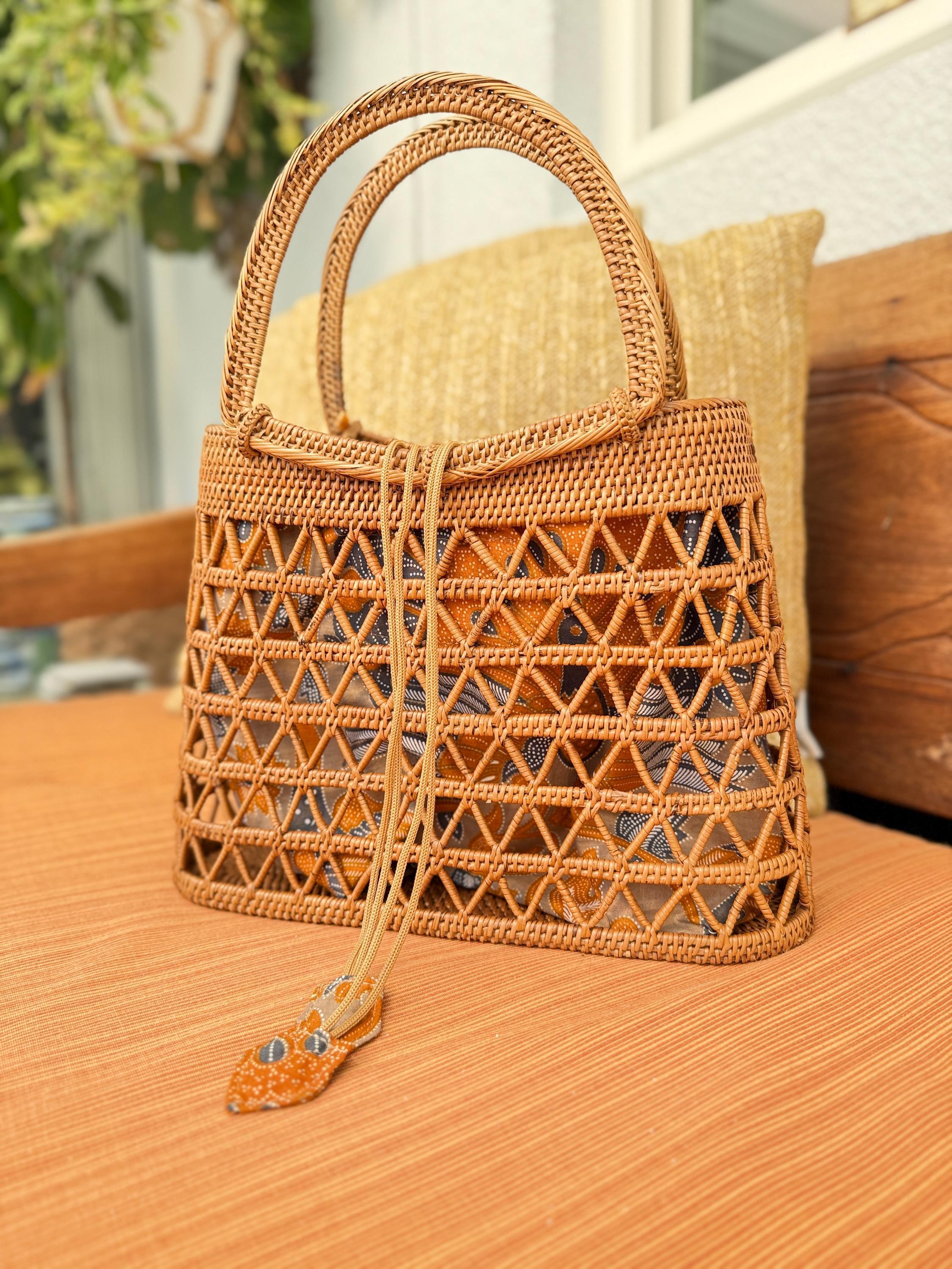 A woven straw handbag with a geometric pattern sits on a wooden surface, with a yellow pillow visible in the background.